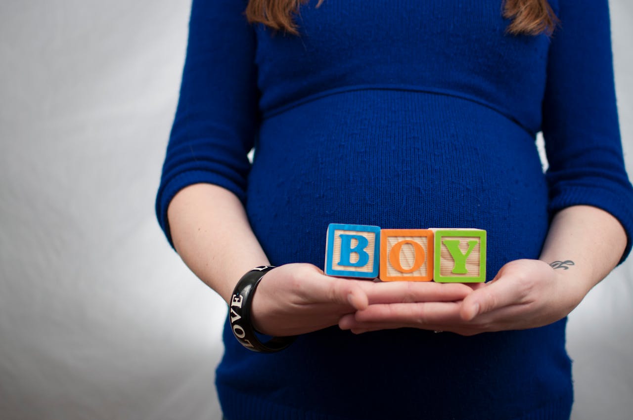 Pregnant woman in blue dress holds 'boy' blocks, symbolizing a baby boy announcement.